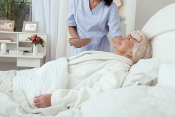 Struggle with fever. Nurse applying compress while inspired elder woman grinning in bed