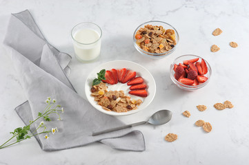 Plate with corn flakes with the addition of fresh strawberry yogurt. Next to the glass with yogurt, cups with cereal and strawberries. Light background. Close-up. 