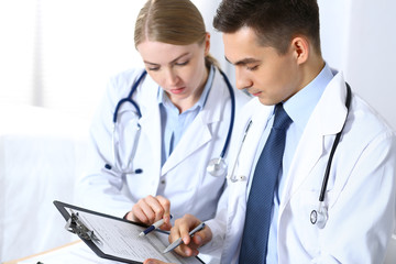 Doctors writing papers using clipboard. Physicians discussing medication program or studying at medical conference. Healthcare, insurance and medicine concept