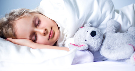 Child little girl sleeps in the bed with a toy teddy bear
