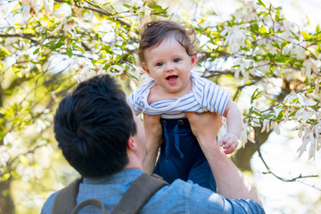 Young father with child have a leisure in springtime flowering garden in sunny day.