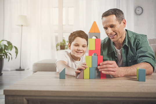 Happy man and boy are playing together at home. They are building toy tower and laughing. Friendly family concept