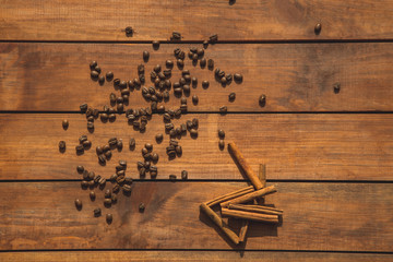 Top view close up aromatic a coffee beans locating near appetizing cinnamon sticks on wooden surface