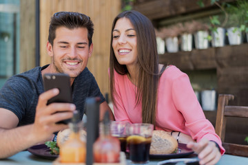 Happy young couple seating in a restaurant with a smartphone