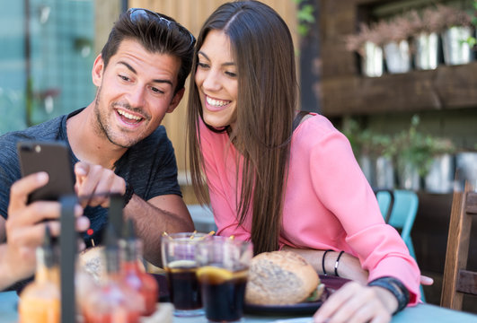 Happy young couple seating in a restaurant terrace with a smartphone