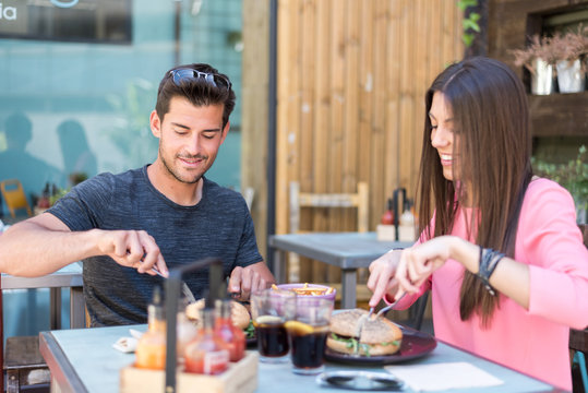 Happy young couple seating in a restaurant terrace eating a burger