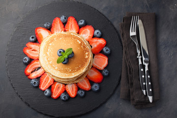 Delicious pancakes close up, with fresh blueberries, strawberries on a black stone background. Top view