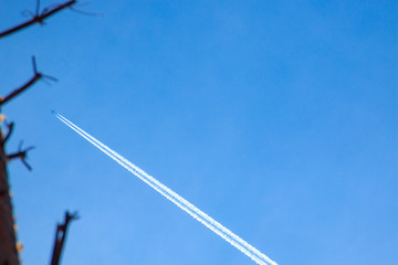 Condensation trace, reactive track - visible trace emerging in atmosphere behind moving aircraft under certain atmospheric conditions against background of tree tops