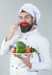 Male chef in white uniform holds pepper beside face. Healthy nutrition and cuisine concept. Bearded chef isolated on white background. Cooking and vegetarian diet concept.