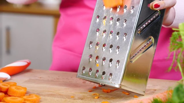 Close up of woman hand grating carrot on kitchen board in slow motion using vegetable grater.