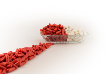 A glass plate with capsules of red color and white tablets, from which stretched a path of red capsules, all on a white background.