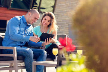 Obraz premium Young couple, woman and man, in street cafe drinking coffee and juice while watching pictures of holidays