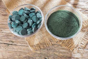 Spirulina powder and tablets on wooden background
