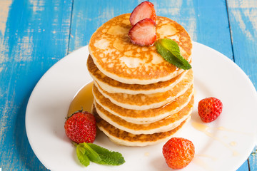 Stack of pancakes (fritters) with strawberries and honey on a plate.