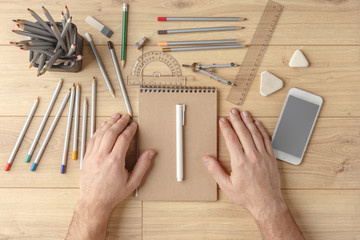 The designer draws a sketch in a notebook on a wooden table. Stationery. View from above.