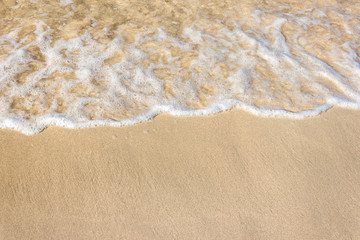 Soft waves with foam of ocean on the sandy beach background