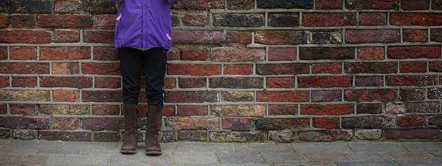 Some part of body child little girl standing up at a brown tone grunge brick wall in the autumn.