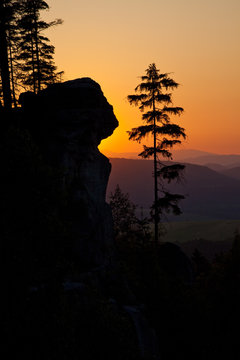 A silhouetted sandstone cliff and trees at sunset on Ostas hill in northern Czech Republic