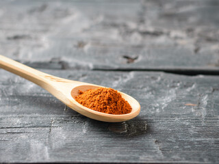 Spoon light wood with crushed red pepper on a dark wooden table.