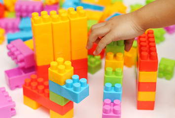Child's hand building plastic toy blocks with blurred background