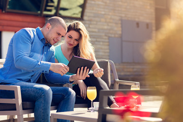 Young couple, woman and man, in street cafe drinking coffee and juice while watching pictures of...