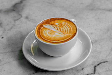 The hot coffee art in the white ceramic mug in the restaurant or coffee shop on the white or gray marble surface.