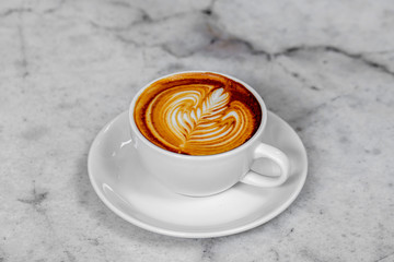 The hot coffee art in the white ceramic mug in the restaurant or coffee shop on the white or gray marble surface.