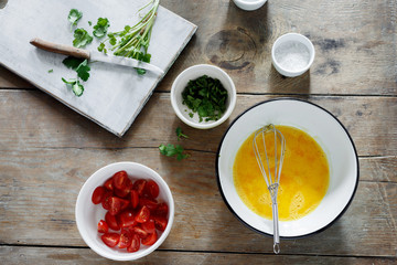 Ingredients for preparation omelette with tomatoes and greenery on wooden table, top view. Rustic style, healthy breakfast concept