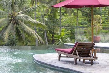 Red umbrella and beach chairs around outdoor swimming pool in hotel and resort with palm tree on island Bali, Indonesia