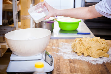 Close-up of a woman baker pouring a large spoon of white flour into a basin. Baker works with flour