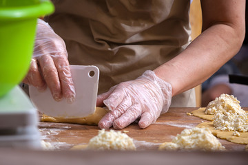 A close-up of a baker in a poor apron sculpts a hot dog bun on a wooden table in a bakery