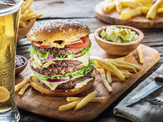 Big hamburger and French fries on the wooden tray.