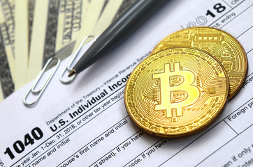 The pen, bitcoins and dollar bills is lies on the tax form 1040 U.S. Individual Income Tax Return. The time to pay taxes