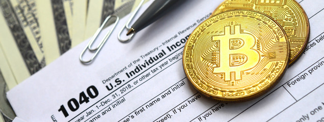 The pen, bitcoins and dollar bills is lies on the tax form 1040 U.S. Individual Income Tax Return. The time to pay taxes