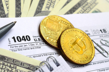 The pen, bitcoins and dollar bills is lies on the tax form 1040 U.S. Individual Income Tax Return....