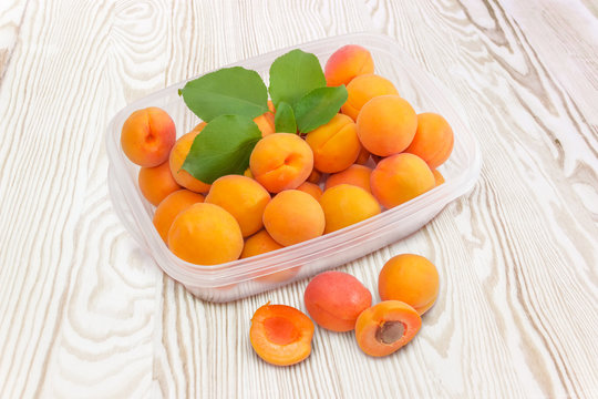 Apricots in container and beside to him on wooden surface