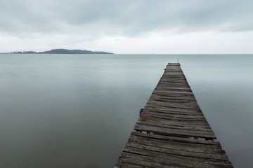 Obraz premium Long exposure first person view of a pier on a lake, with a tree