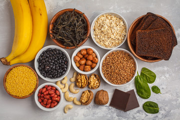 Healthy food nutrition dieting concept. Assortment of high magnesium sources. Banana chocolate spinach, buckwheat, nuts, beans, oat. White background, top view - obrazy, fototapety, plakaty