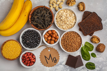 Healthy food nutrition dieting concept. Assortment of high magnesium sources. Banana chocolate spinach, buckwheat, nuts, beans, oat. White background, top view