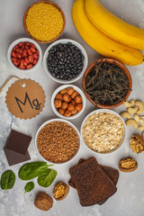 Healthy food nutrition dieting concept. Assortment of high magnesium sources. Banana chocolate spinach, buckwheat, nuts, beans, oat. White background, top view