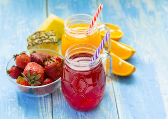 Fresh pineapple and strawberry smoothie in glasses with fruits on a blue wooden rustic background