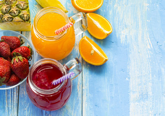 Fresh pineapple and strawberry smoothie in glasses with fruits on a blue wooden rustic background