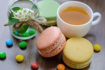 Mug of hot herbal tea, sweets (marmalade, candy, chocolate, cookies, pastries, dessert) and a decorative jar of flowers on a blue wooden table.