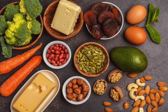 Healthy food nutrition dieting concept. Assortment of high vitamin A sources. Carrots, nuts, broccoli, butter, cheese, avocado, apricots, seeds, eggs. Dark background, copy space