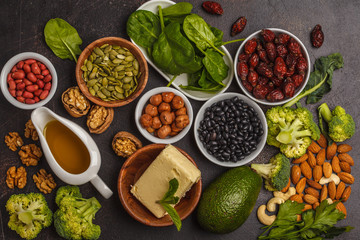 Healthy food nutrition dieting concept. Assortment of high vitamin E sources. Oil, nuts, avocado, butter, healthy fats, rose hips, parsley, seeds, spinach. Dark background, top view