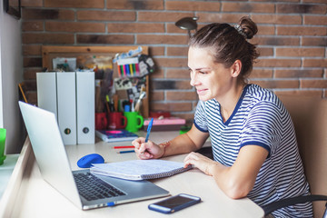 Girl student freelancer working with laptop at home by the window, education and remote work,...