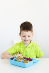 One young boy sitting, looking at his lunch box. white background. Closeup