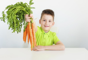Lovely young boy holds a carrot in his hand. White background. Closeup of carrot