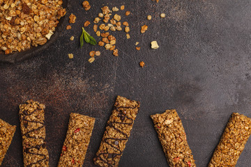 Granola bars and ingredients. Healthy sweet dessert snack. Cereal granola bar with nuts, chocolate  and berries on a dark background. Top view, copy space.