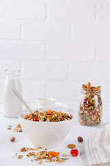 Healthy breakfast concept. Baked granola in white ceramic bowl and glass jar on the kitchen table.